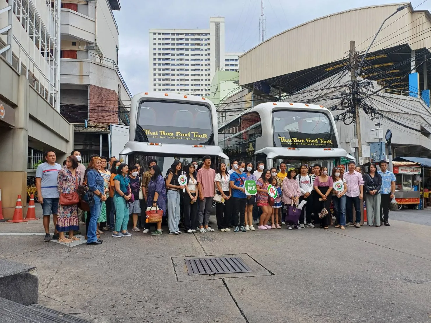 Large group of tour participants in colorful clothing standing in front of Thai Bus Food Tour buses