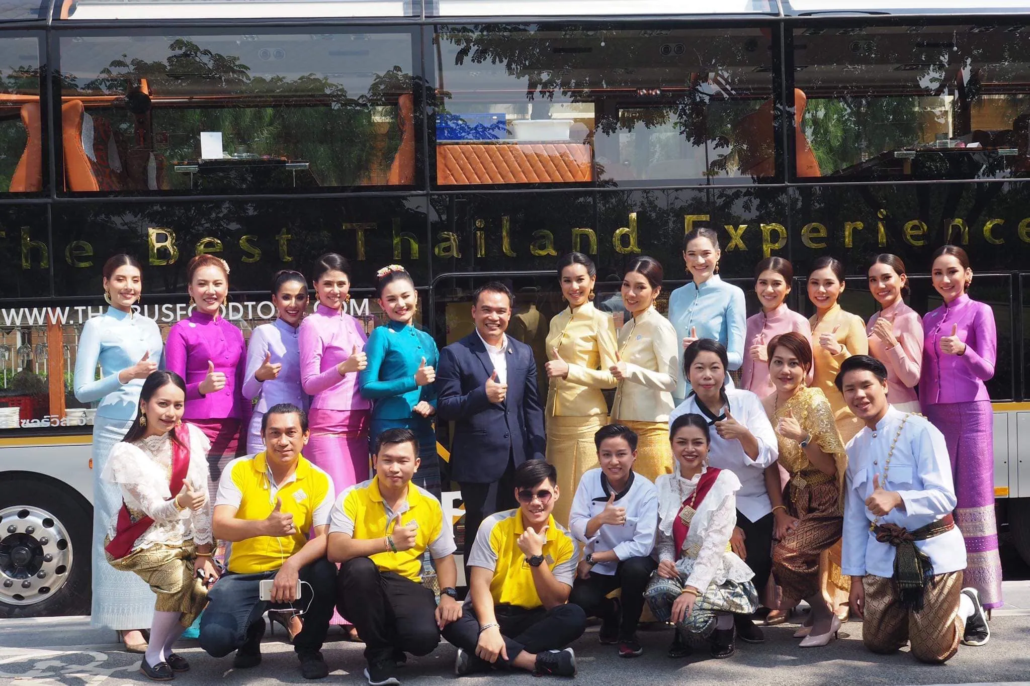 Large group of tour participants in various colored outfits posing together outside bus