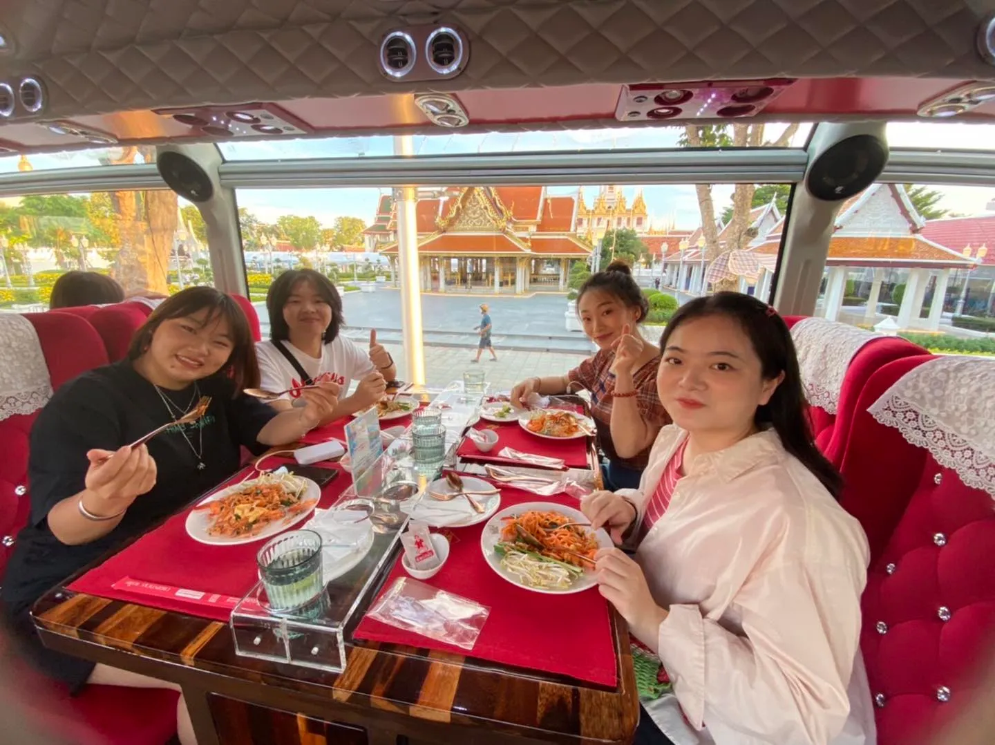 Group of four female guests smiling while eating dishes beside river with stilt houses