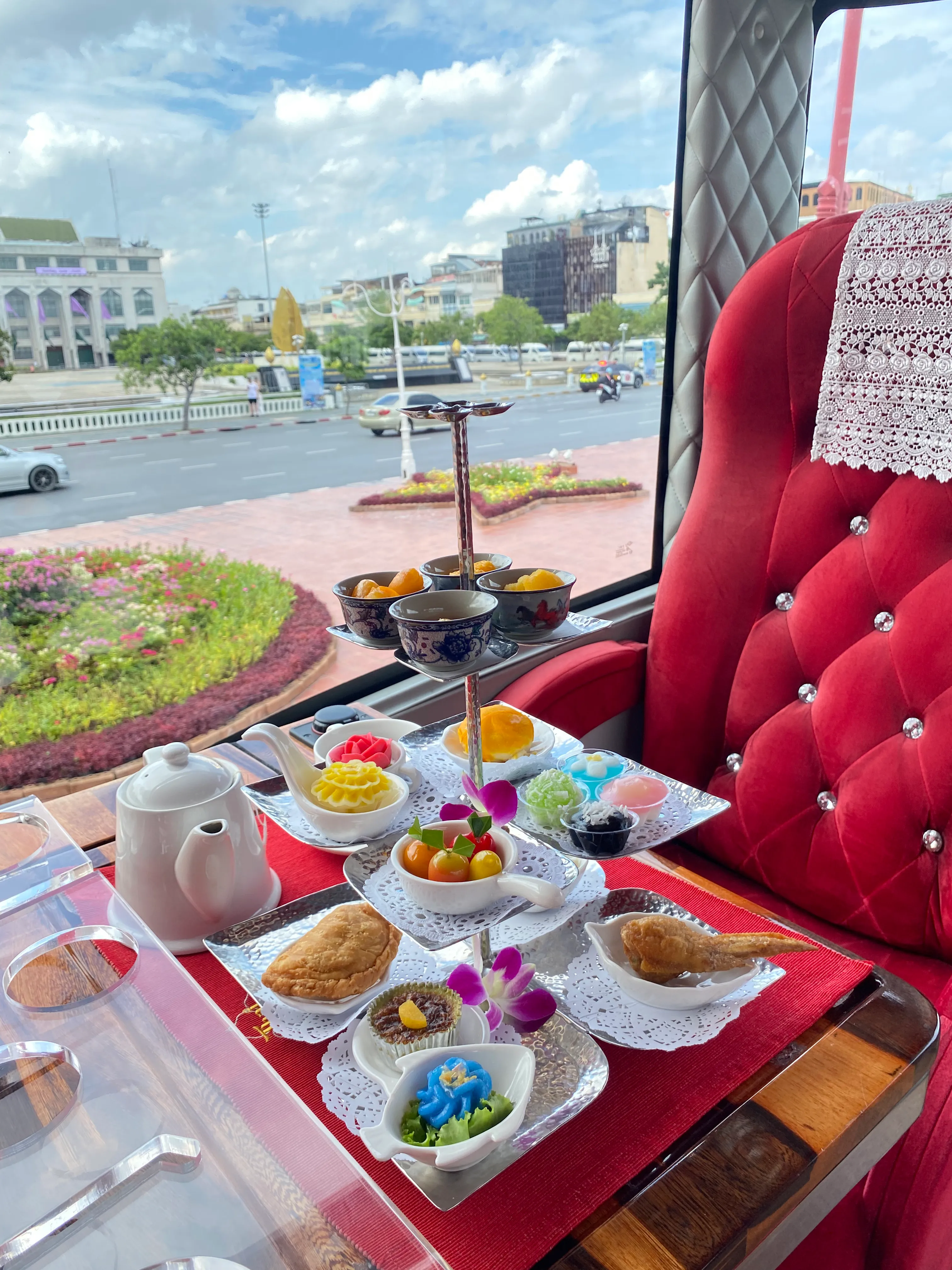 Elegant afternoon tea set with Thai sweets and Mont Nom Sod toast served at a window table on the Thai Bus Food Tour, the Giant Swing visible outside