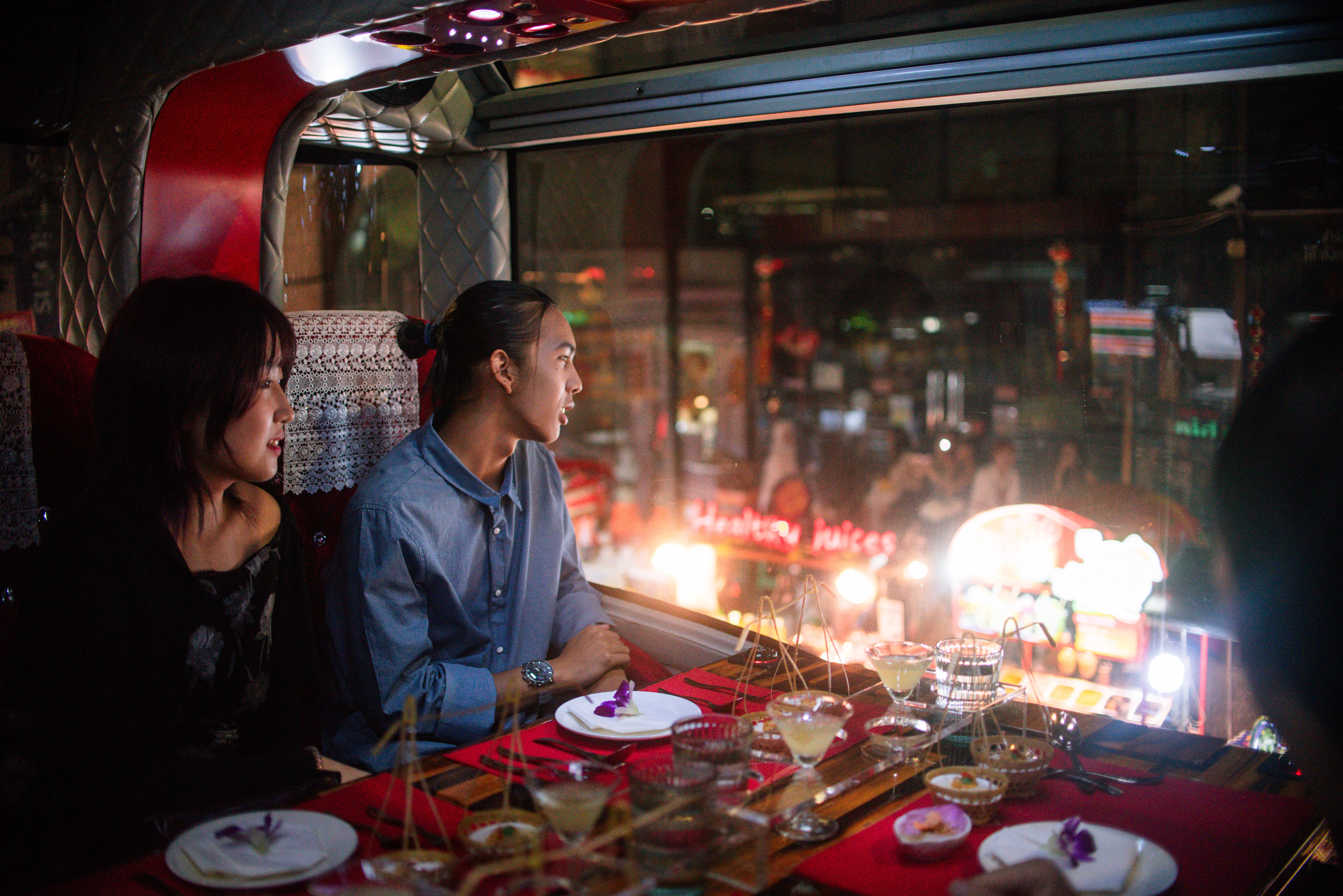 Colourful vegetarian Thai dishes served at a table aboard the Thai Bus Food Tour double-decker, with Wat Arun visible through the window at sunset