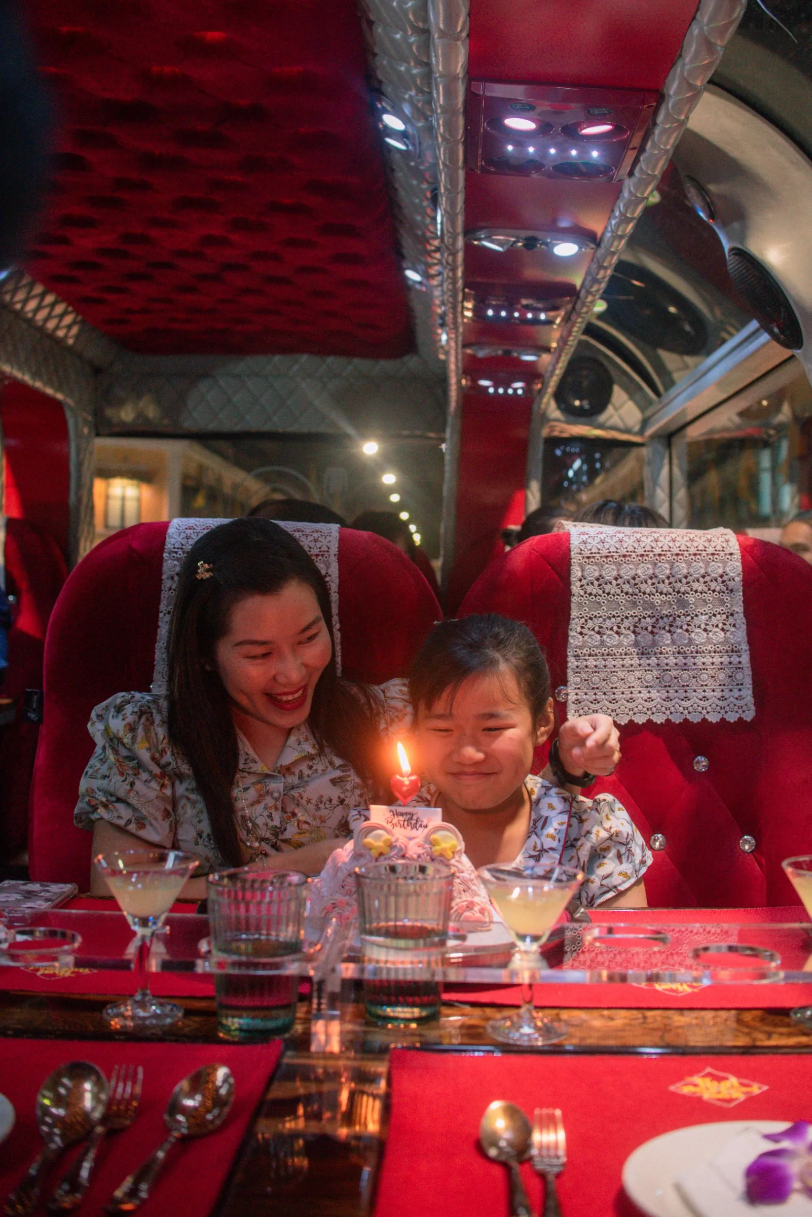 Group of friends celebrating at a table aboard the Thai Bus Food Tour double-decker with Bangkok landmarks lit up outside the window